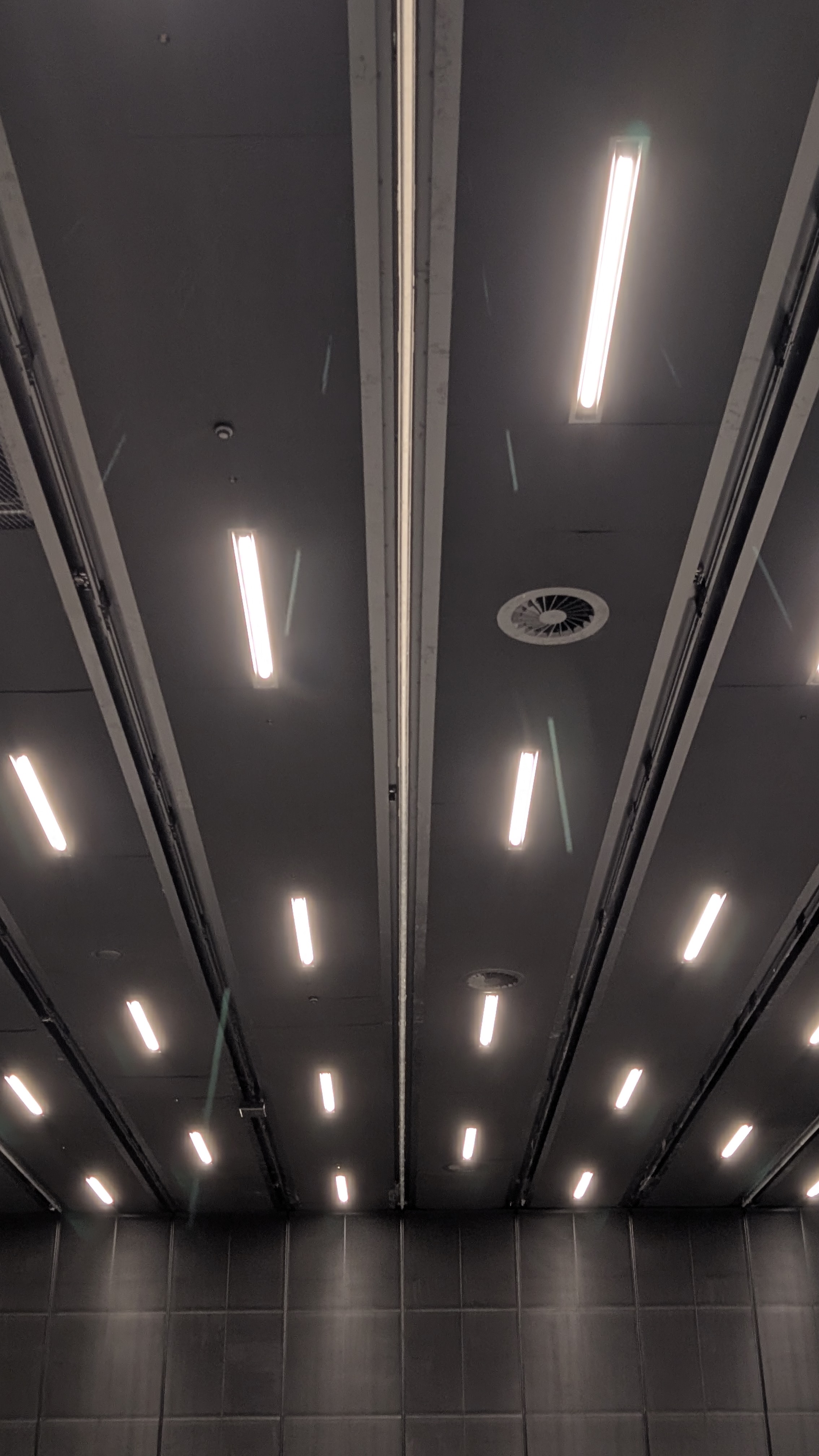 Looking up at the finished dark ceiling with recessed rail lines and linear lighting running away from the camera